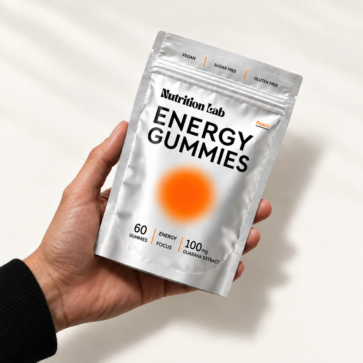 An adult hand holding the Nutrition Lab Energy Gummies peach pouch in soft daylight.